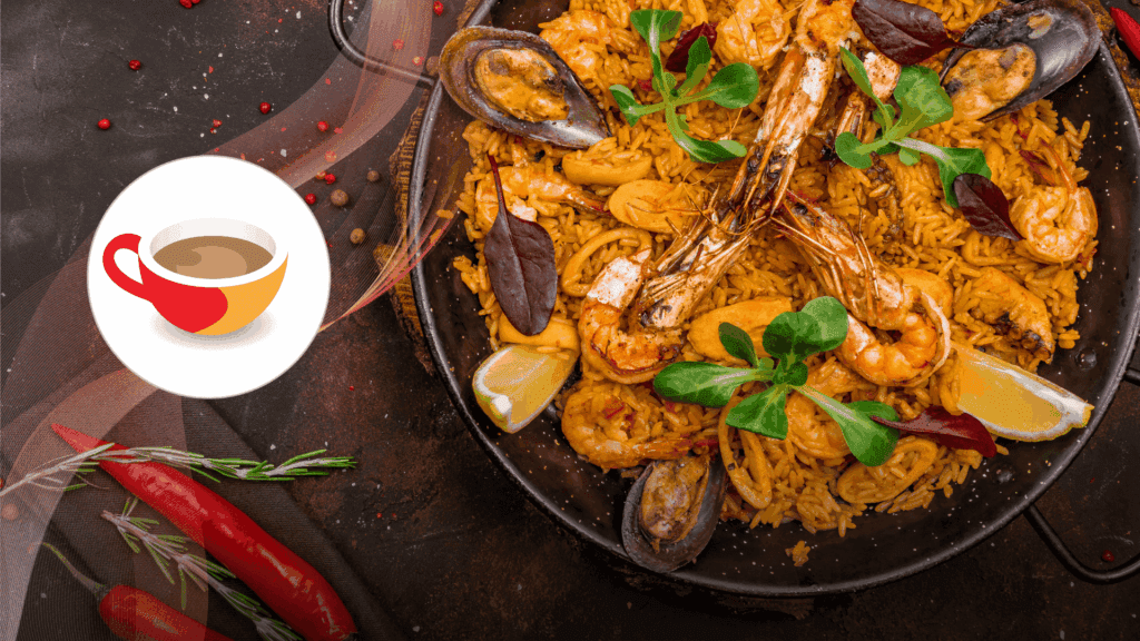 A close-up of a seafood paella in a black pan, featuring shrimp, mussels, rice, lemon wedges, and fresh greens