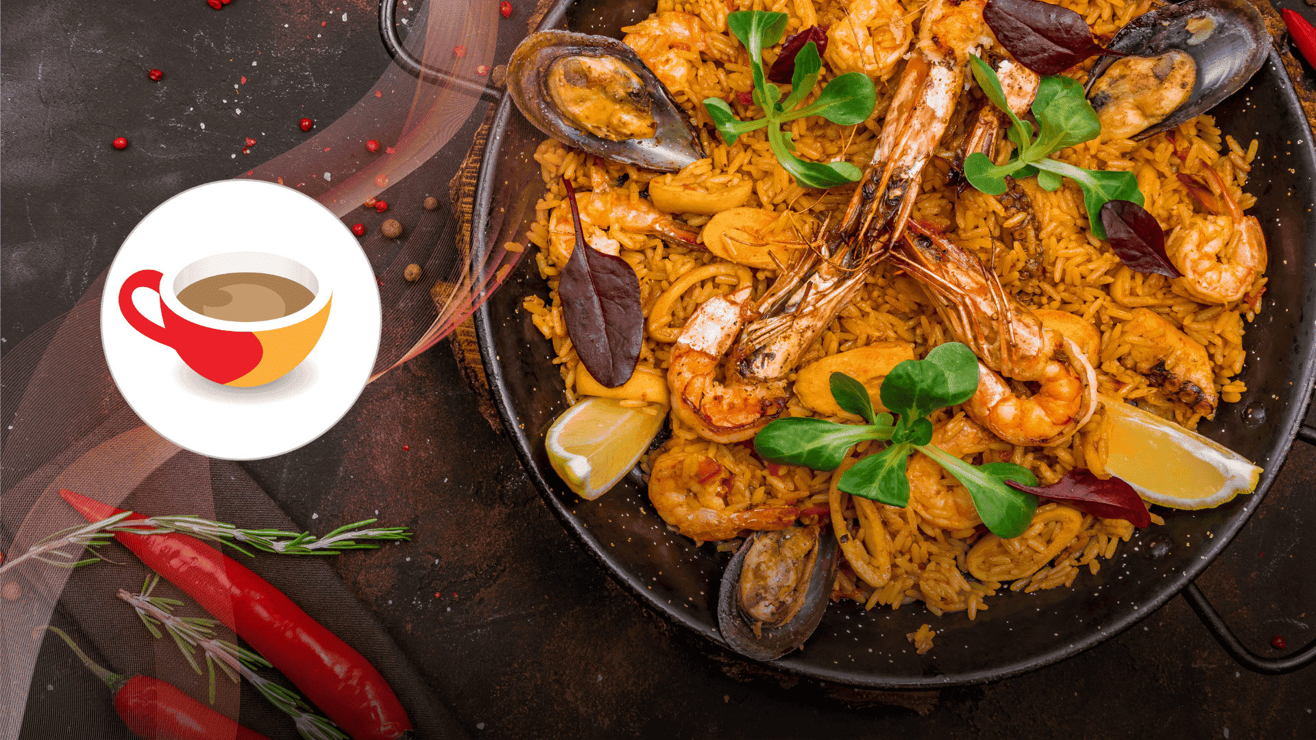 A close-up of a seafood paella in a black pan, featuring shrimp, mussels, rice, lemon wedges, and fresh greens