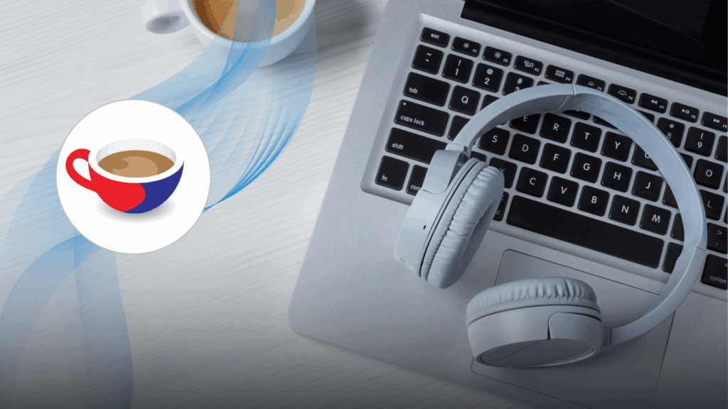 Close-up of a laptop keyboard with a pair of white over-ear headphones resting on it, alongside a cup of espresso on a white wooden desk.