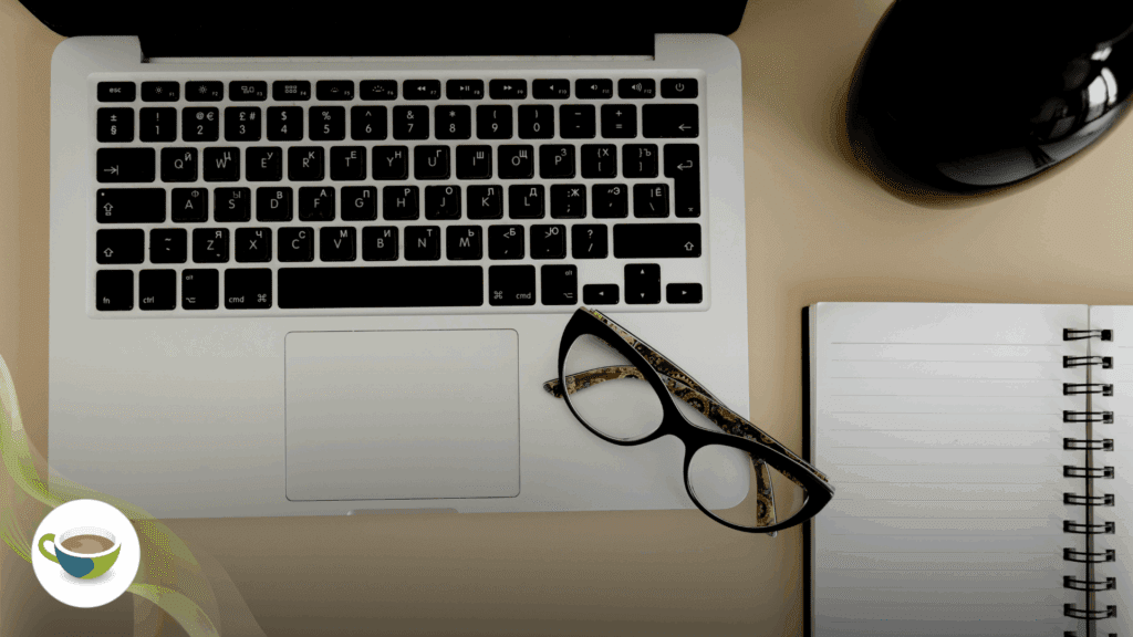 Laptop resting on top of a table with glasses and a notebook close to it.