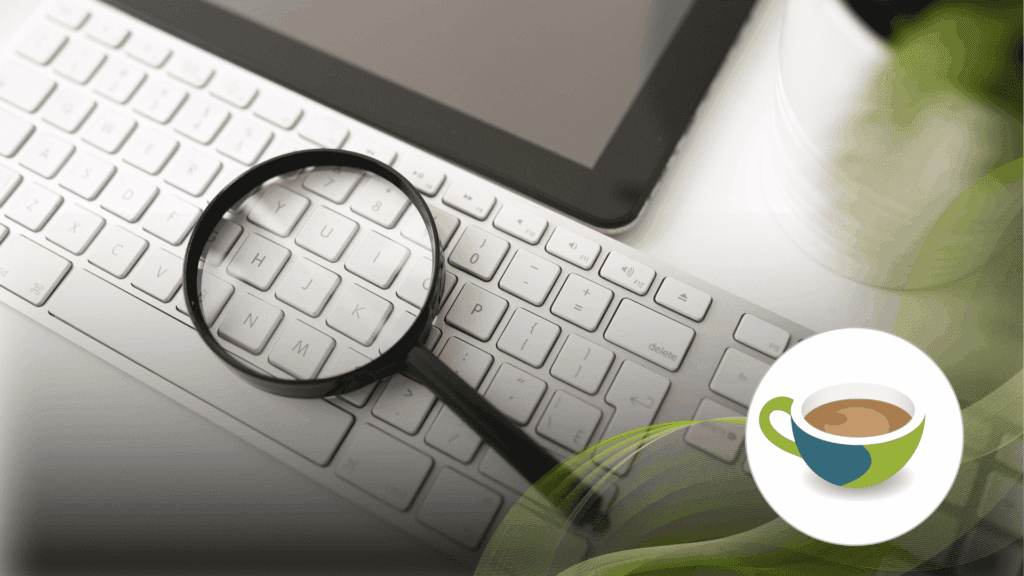 A magnifying glass resting on a white keyboard beside a tablet.