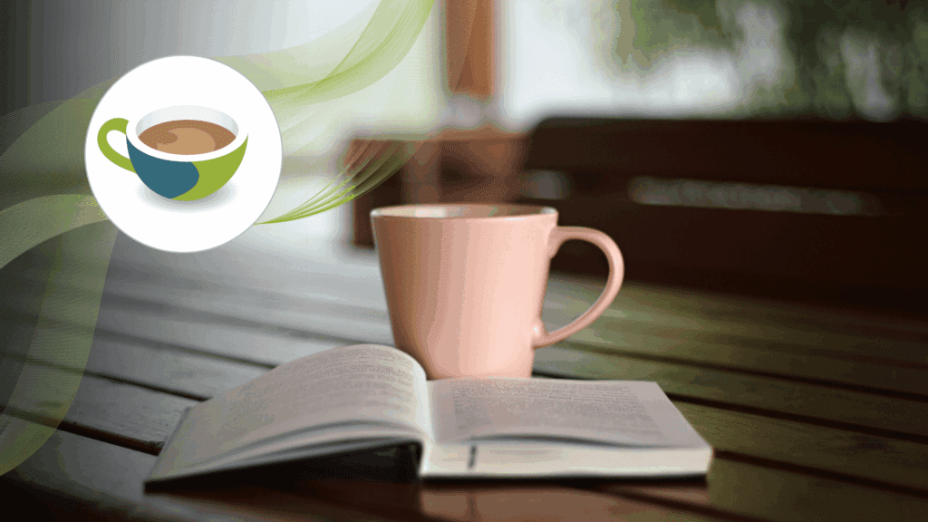 Open book and a pink coffee mug on a wooden table, with a blurred background of greenery and benches.