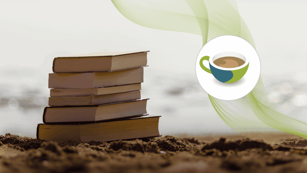 A stack of books resting on sand by the seashore, suggesting a relaxed summer reading scene.