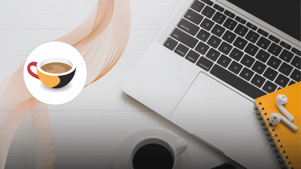 “A laptop keyboard on a white desk next to a yellow notebook with wireless earbuds and a cup of coffee.