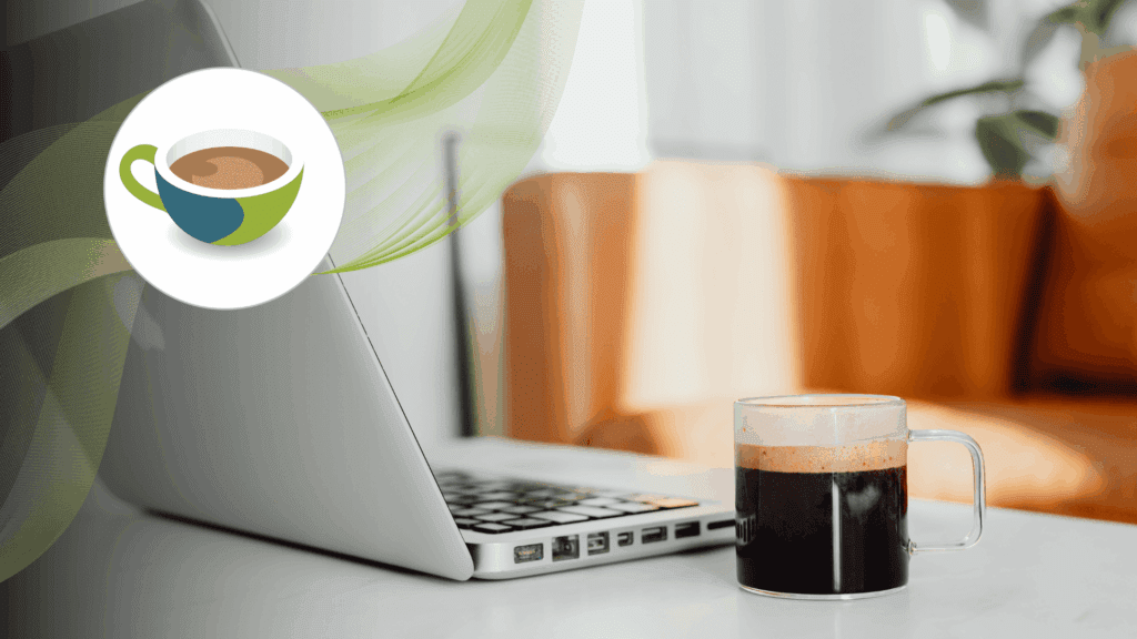 Laptop keyboard with a takeaway cup of frothy coffee on a small round table, alongside a wooden décor piece.
