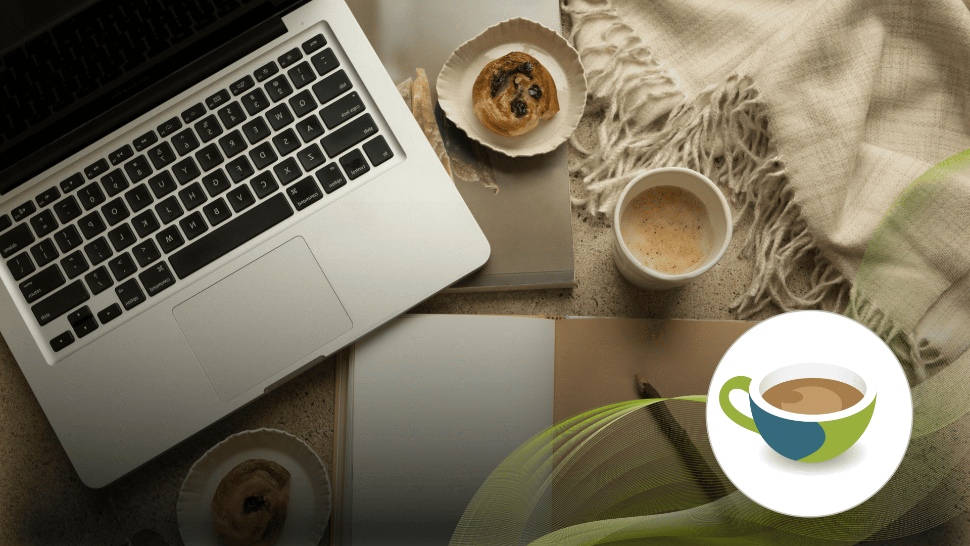 Cosy workspace with a laptop, notebook, coffee cup, and pastries on a textured surface, with a soft blanket.